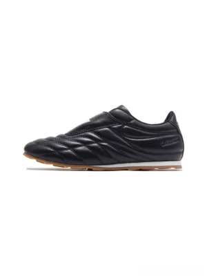 Side view of black quilted soccer trainer sneaker with fold-over graphic strap and slim gum rubber sole