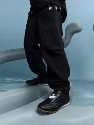 Black quilted leather soccer trainer sneakers styled with black cargo pants in a minimalist setting