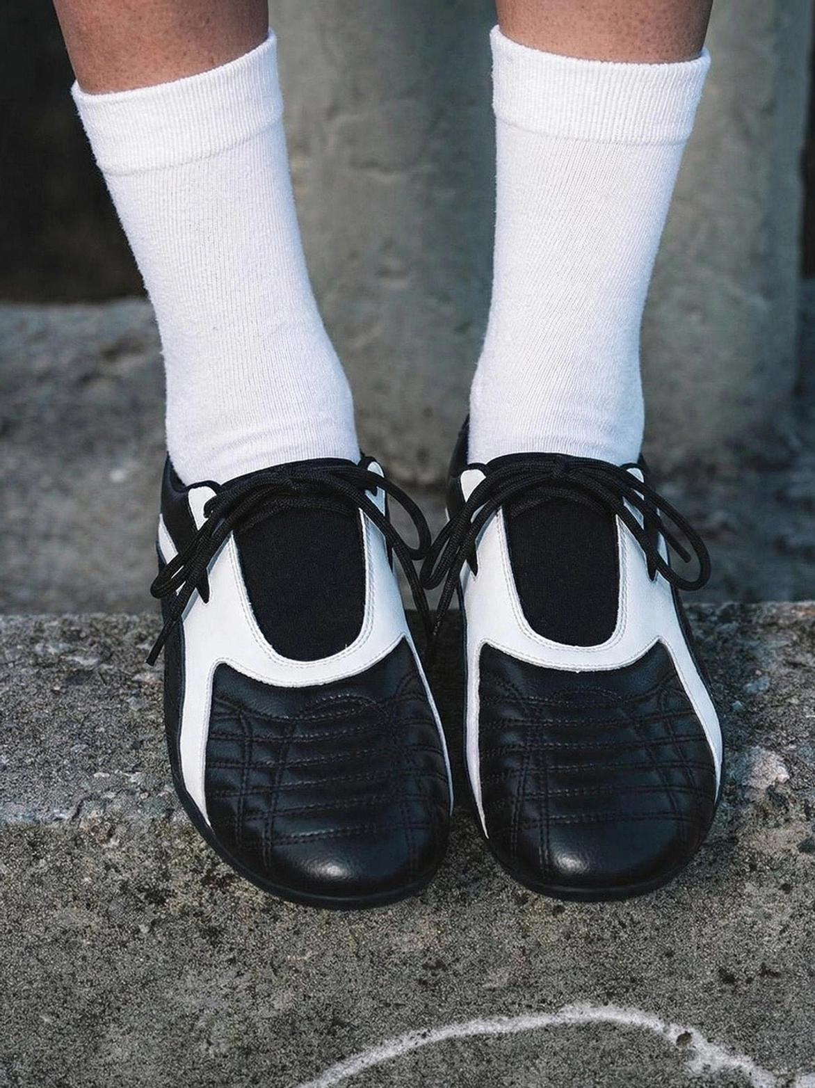 Top-down view of black quilted toe sneakers with white center panels, black flat laces, and a clean low-profile flat sole