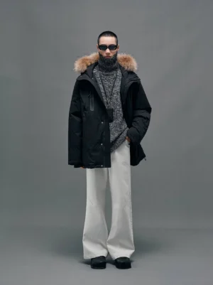 Black hooded down coat with plush raccoon fur collar shown in a full front studio outfit with white wide-leg trousers