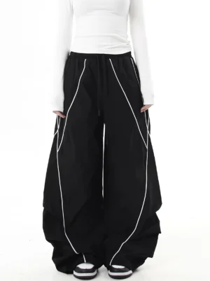 Front view of black reflective curve-leg wide-leg cargo pants styled with a white long-sleeve shirt and sneakers, showing diagonal reflective piping, elastic drawstring waist, and relaxed streetwear fit