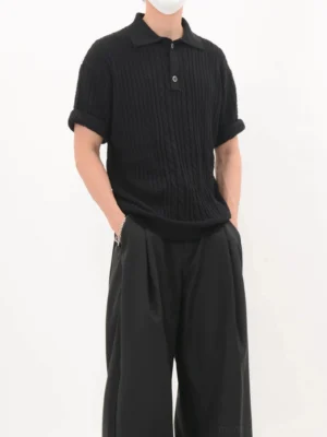 Black relaxed cable knit polo shirt shown from a three-quarter angle with textured vertical knit ridges and wide-leg black pants