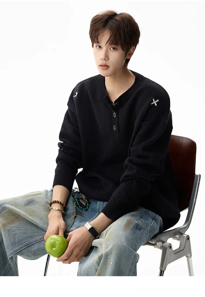 Side view of a black relaxed henley knit sweater showing the long loose sleeves, classic button neckline, and shoulder embroidery