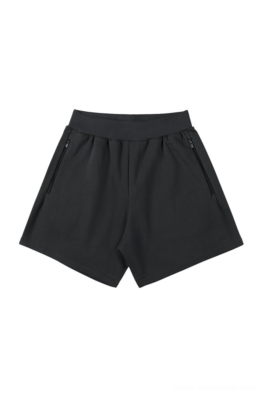 Black relaxed streetwear sweat shorts with elastic ribbed waistband, angled zip pockets, and clean oversized casual athletic fit