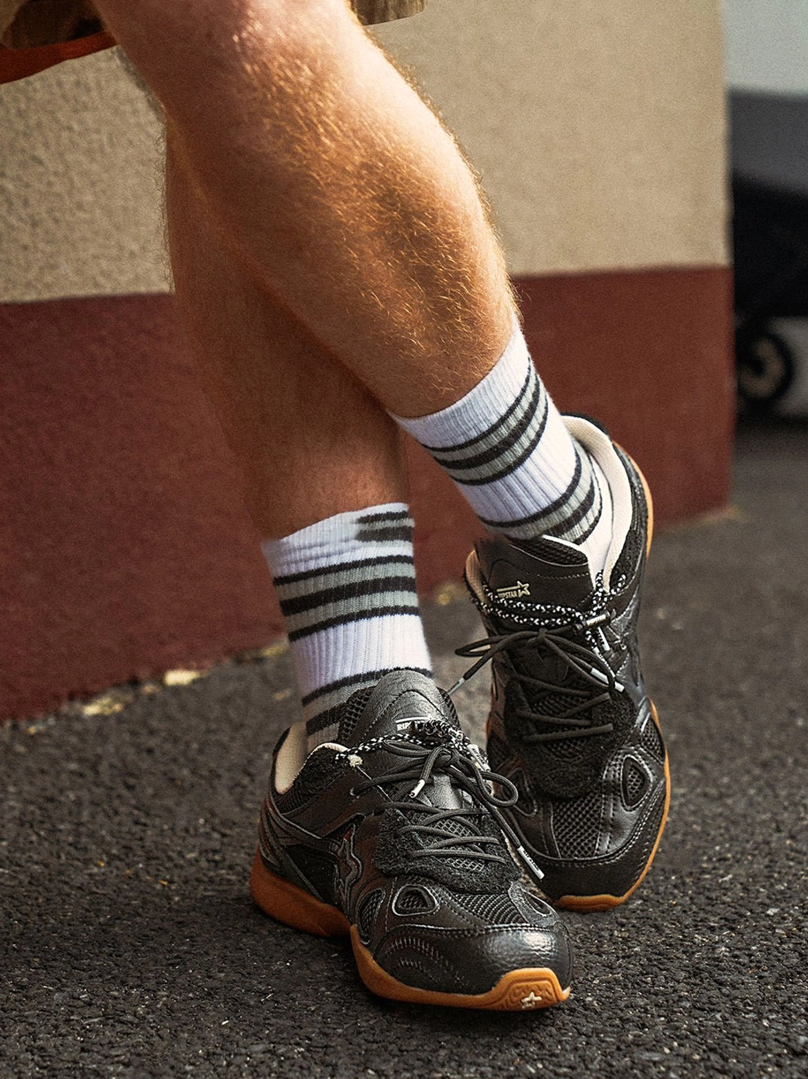 Close-up rear view of black retro runner sneakers worn with black and white striped socks on an outdoor asphalt street