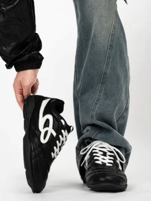 Black retro streetwear sneakers with white script side detail styled with washed baggy jeans and black jacket