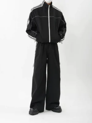 Front view of black zip-up retro stripe track jacket and wide-leg track pants set with white contrast piping and platform shoes