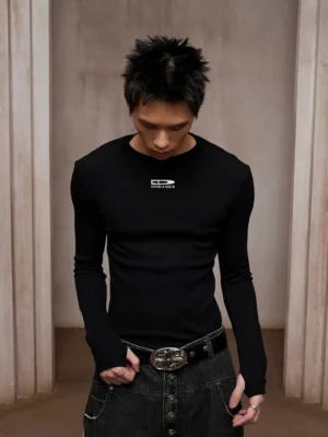 Black ribbed compression long sleeve tee with minimalist chest graphic, slim crew neck fit, and textured stretch fabric styled with dark denim and a metal buckle belt