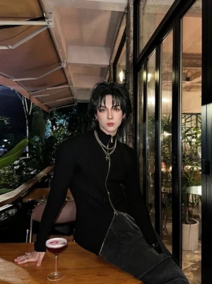 Black ribbed full-zip stand collar streetwear top with slim fitted silhouette styled with layered silver necklaces at a nighttime cafe