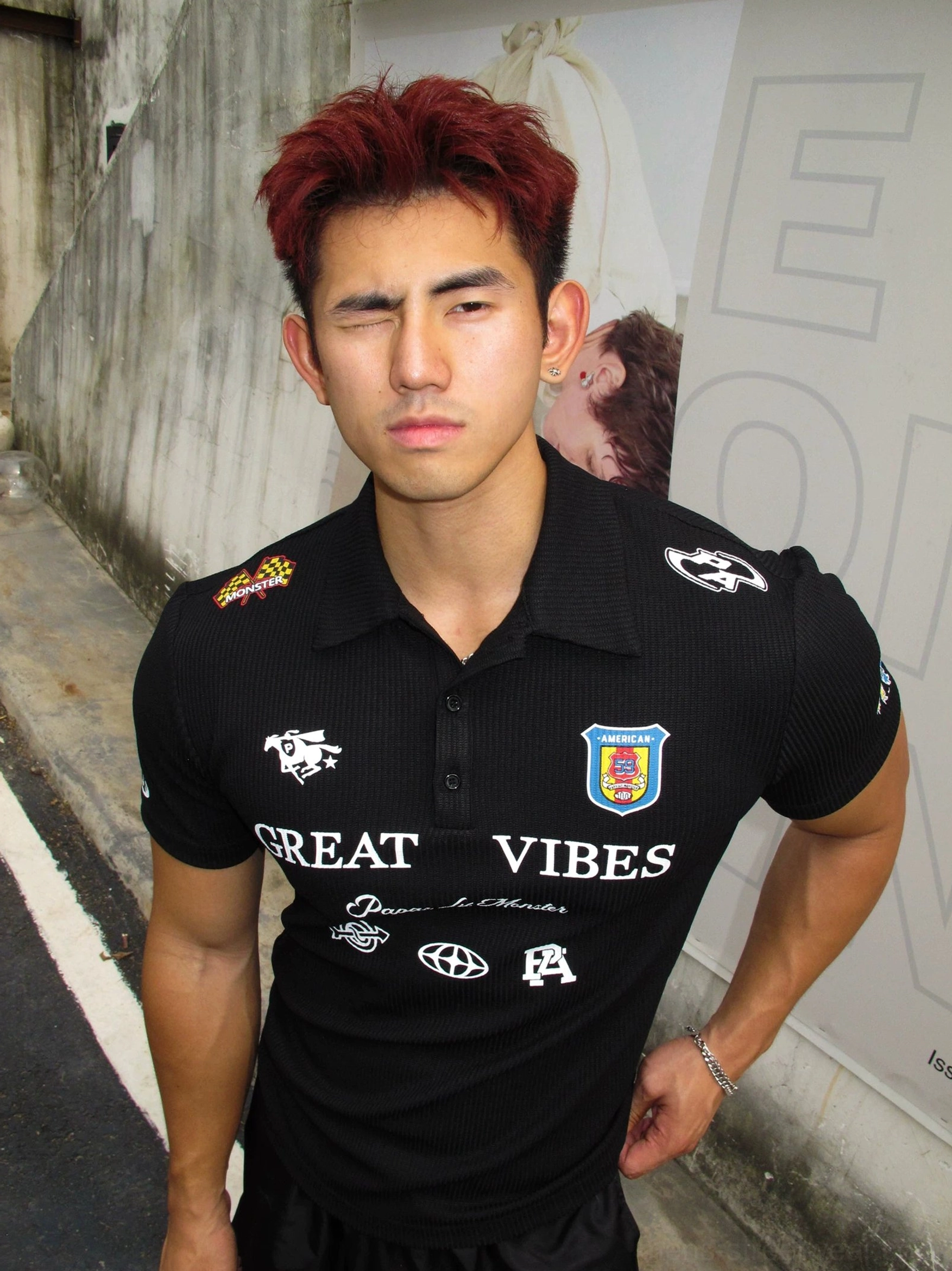 Red-haired male model wearing a black ribbed Great Vibes graphic polo shirt with detailed chest graphics and shoulder badges