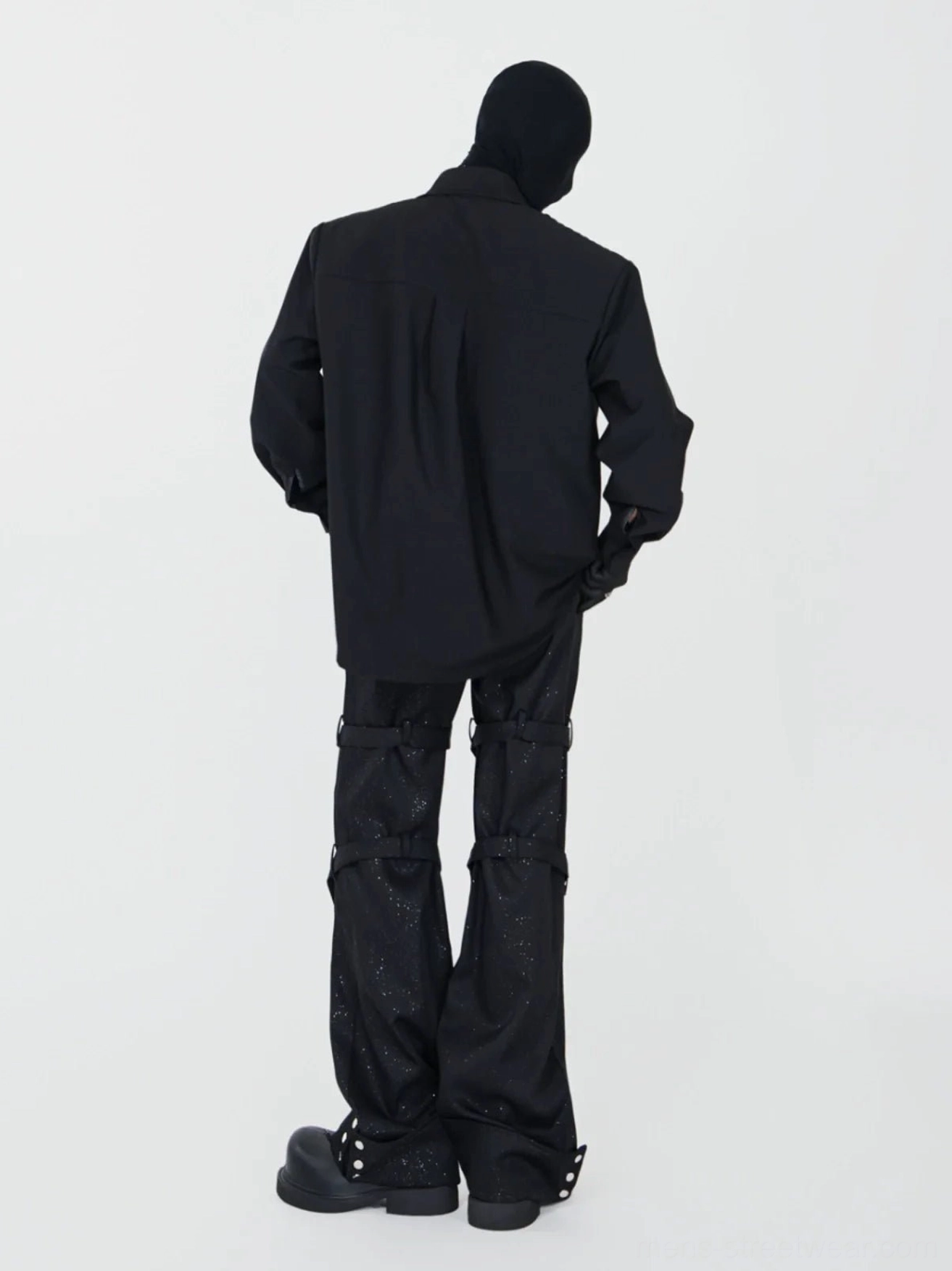 Back view of black rivet spiral flare pants showing leg straps snap fastener cuffs and wide dramatic silhouette