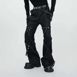 Front low angle view of black glittery rivet spiral flare pants with cross leg straps and silver hardware styled with platform boots
