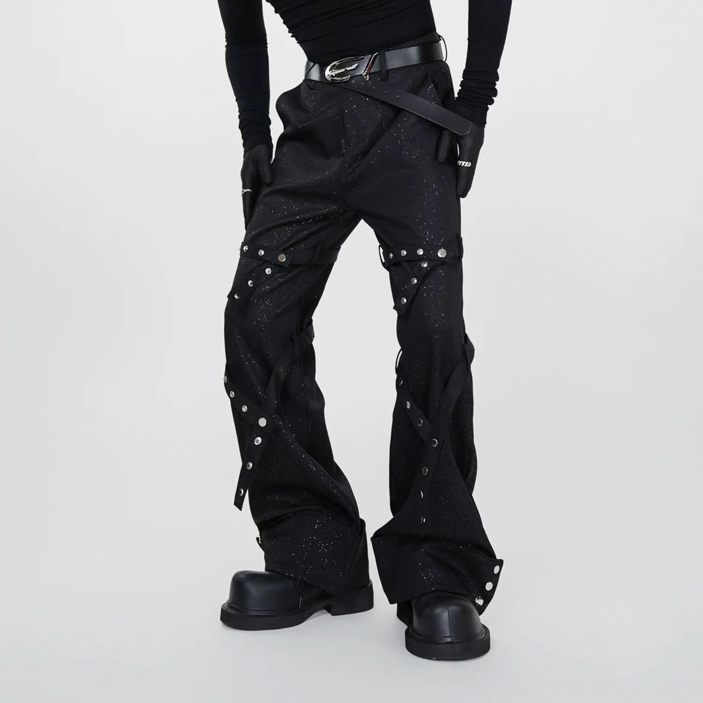 Front low angle view of black glittery rivet spiral flare pants with cross leg straps and silver hardware styled with platform boots