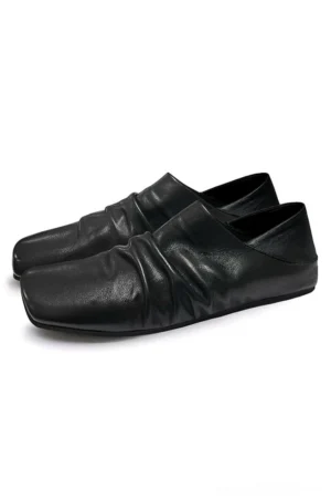 Black ruched leather mules shown in three quarter side view with soft gathered upper and minimalist flat outsole