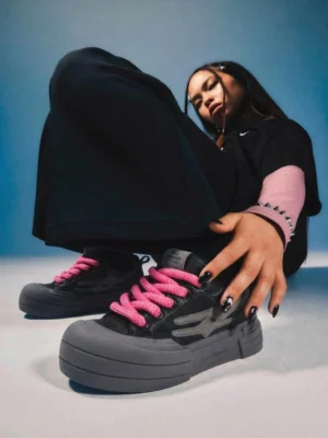 Black chunky platform streetwear sneakers with pink laces styled on a female model in layered urban fashion