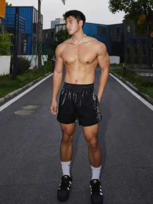 Front full-body view of model wearing black satin logo athletic shorts styled with white socks and black sneakers
