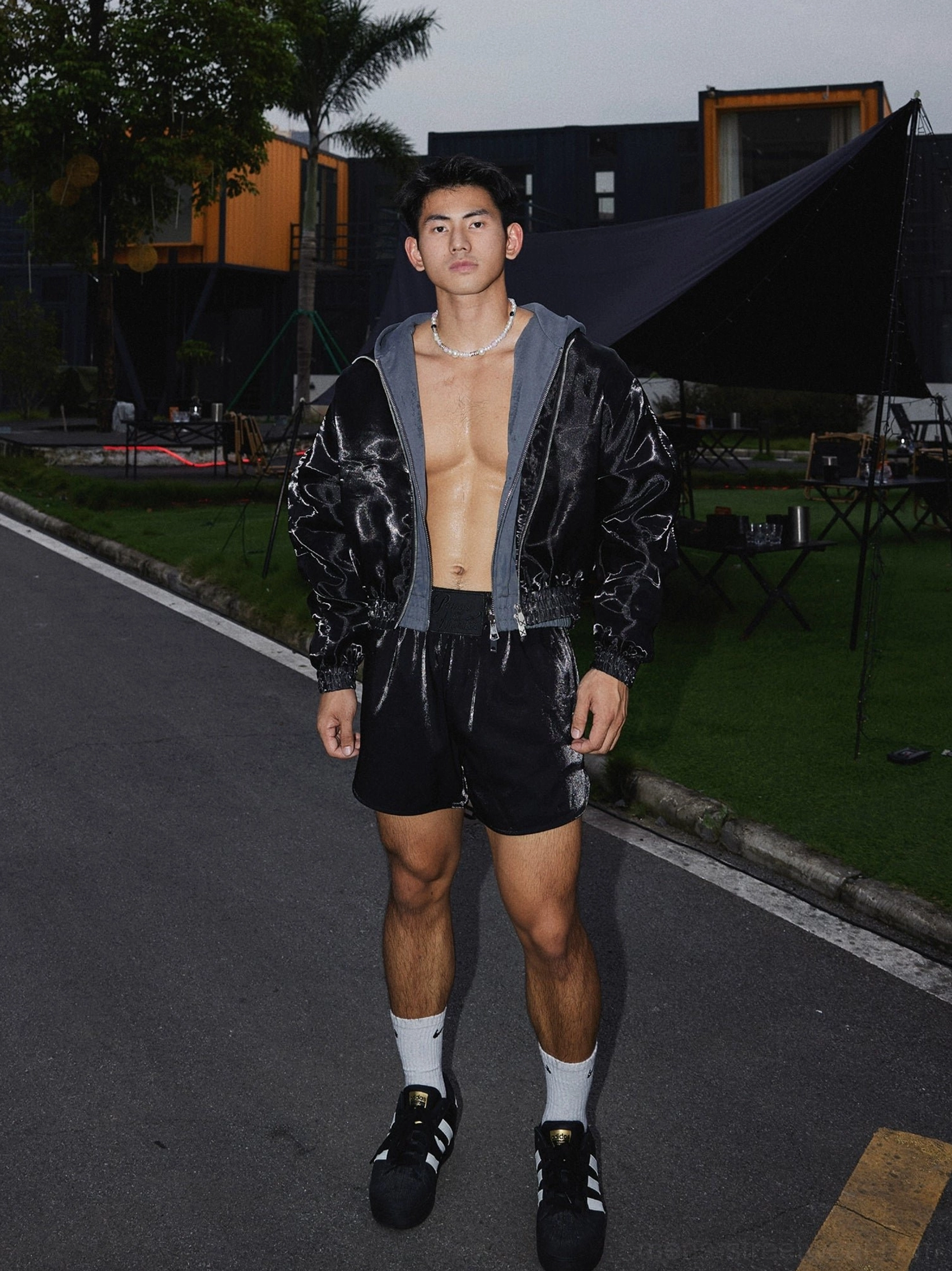Front full-body styling view of loose black satin athletic shorts with black jacket and layered grey top