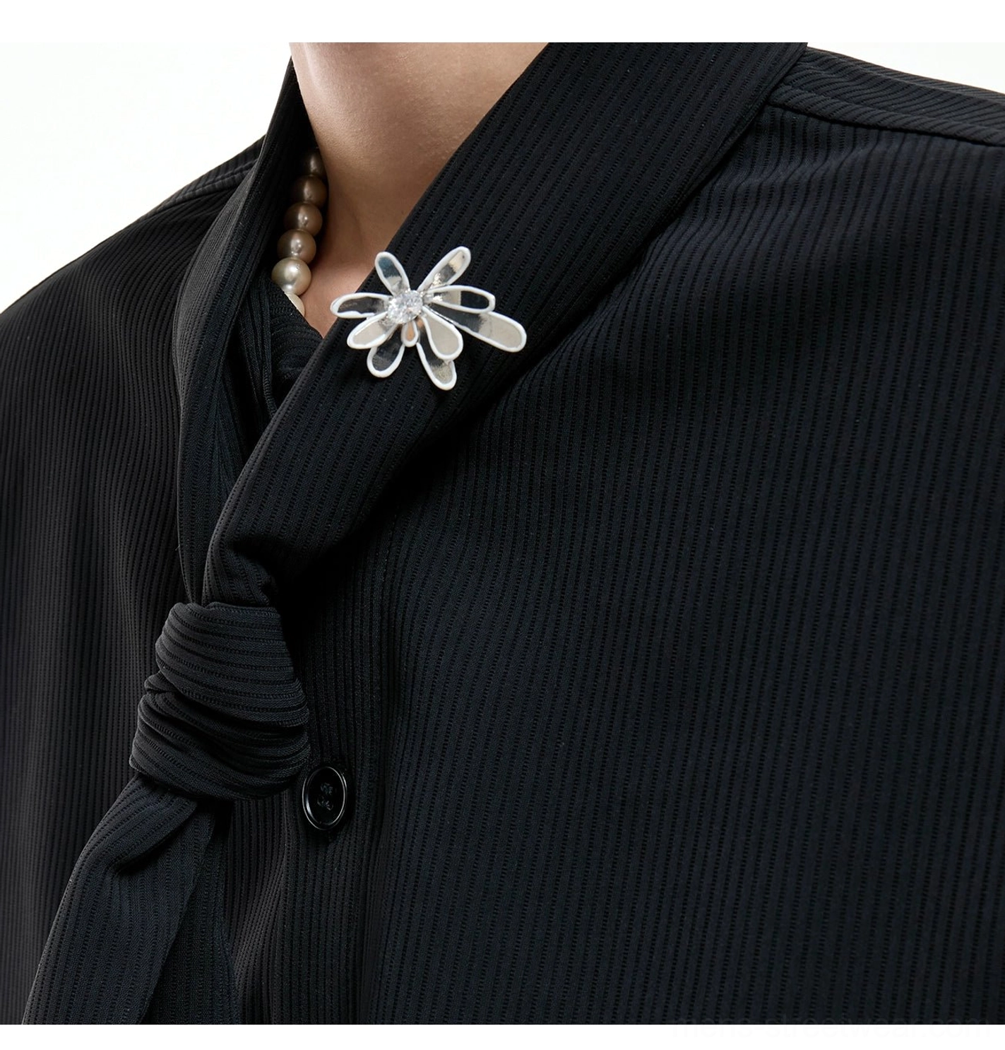 Close-up of black scarf collar suit neckline showing ribbed suiting fabric, knotted scarf detail, round button fastening, and pearl crystal flower brooch