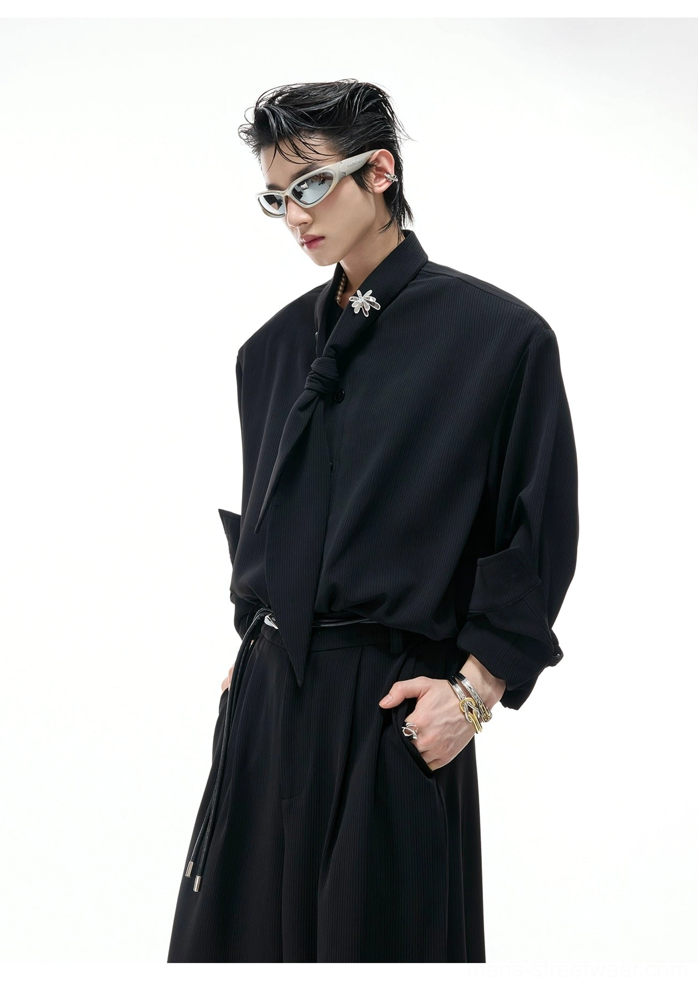 Close-up view of black scarf collar suit top and matching trousers with knotted tie collar, crystal flower brooch, and polished suiting fabric