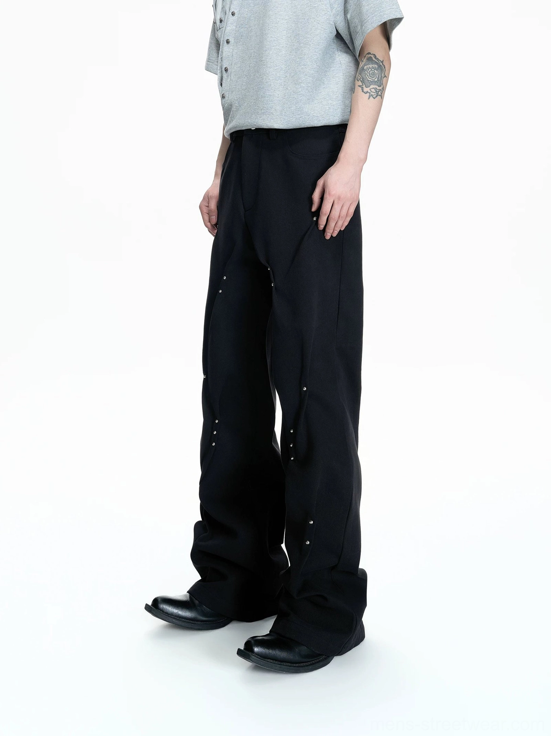 Black flared denim pants three quarter front view with silver rivets sculpted leg seams and wide streetwear fit