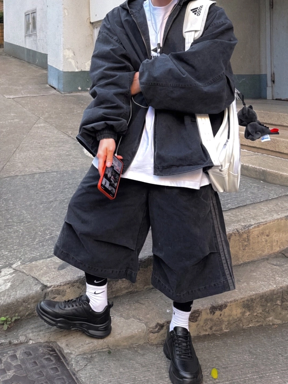 Black chunky leather-look sneakers styled with baggy dark streetwear clothing on outdoor stairs