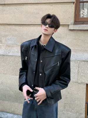Black sculpted wide-shoulder cropped streetwear jacket shown from the front three-quarter view with sunglasses and a silver chain necklace