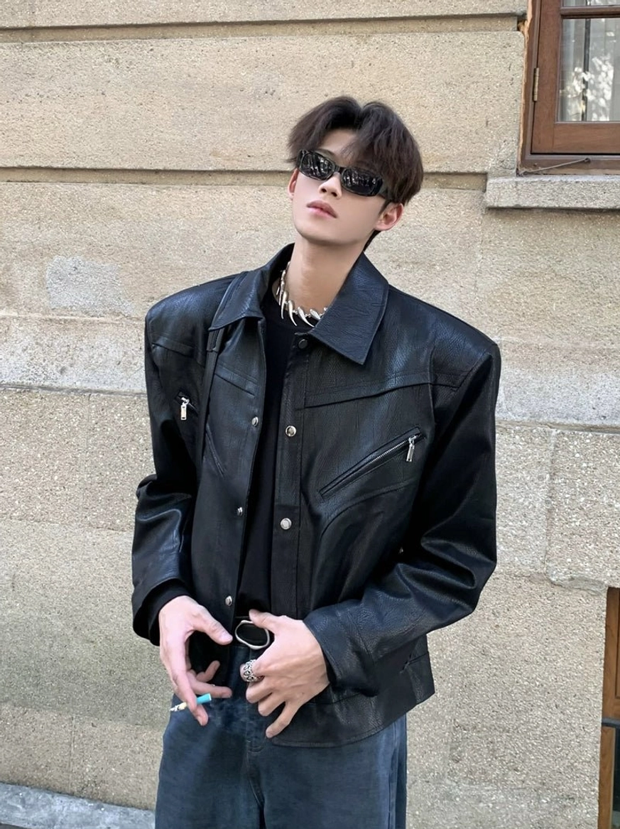 Black sculpted wide-shoulder cropped streetwear jacket shown from the front three-quarter view with sunglasses and a silver chain necklace