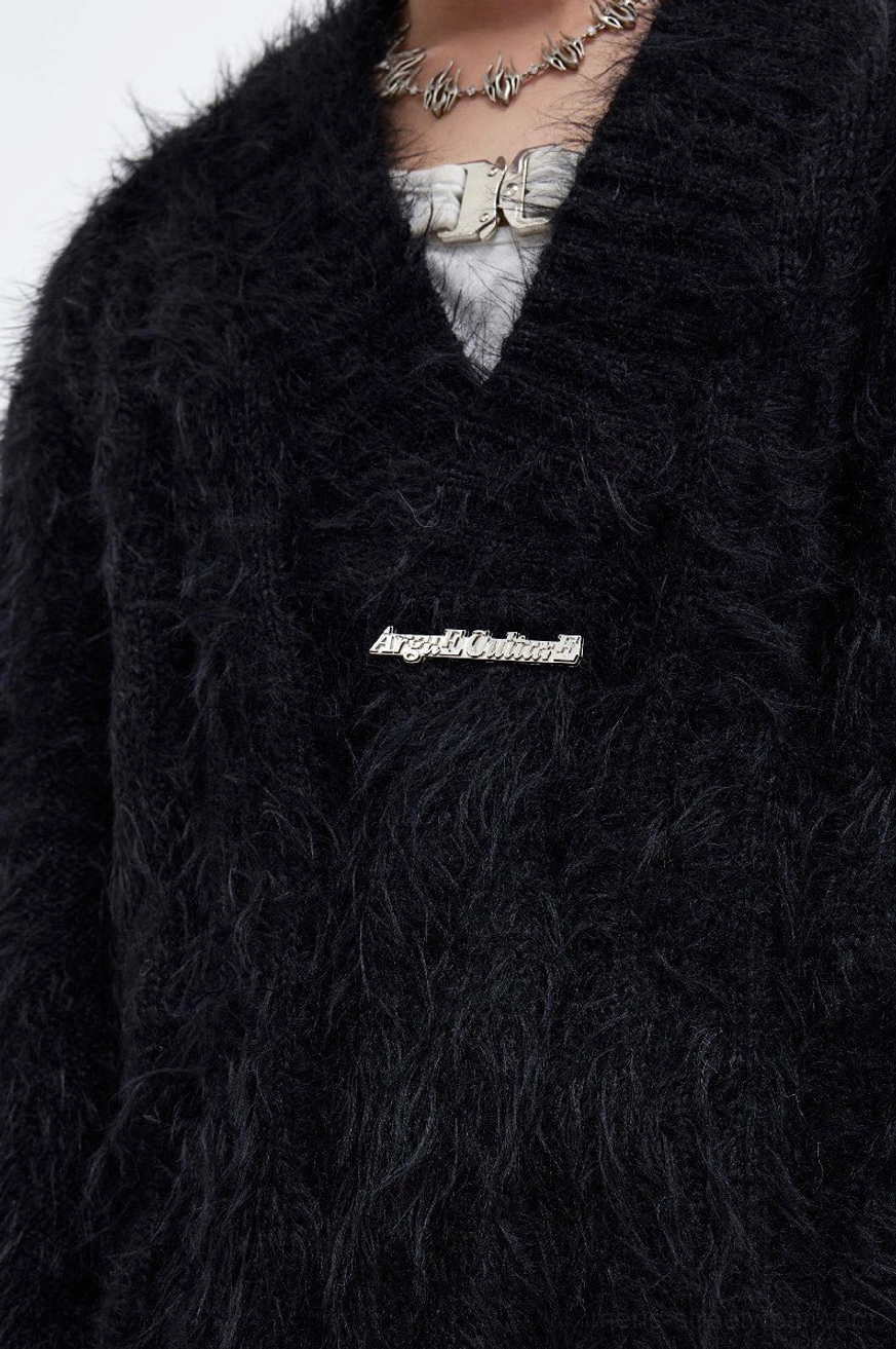 Close-up of black shaggy faux-fur sweater texture with deep V-neck, layered inner top, necklace, and metal front accent