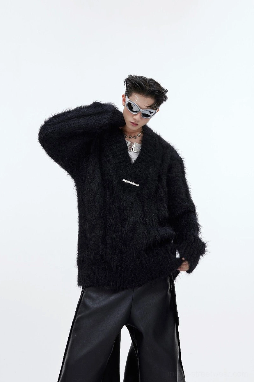 Black shaggy faux-fur V-neck sweater shown from a three-quarter side angle with oversized hem and metal front detail