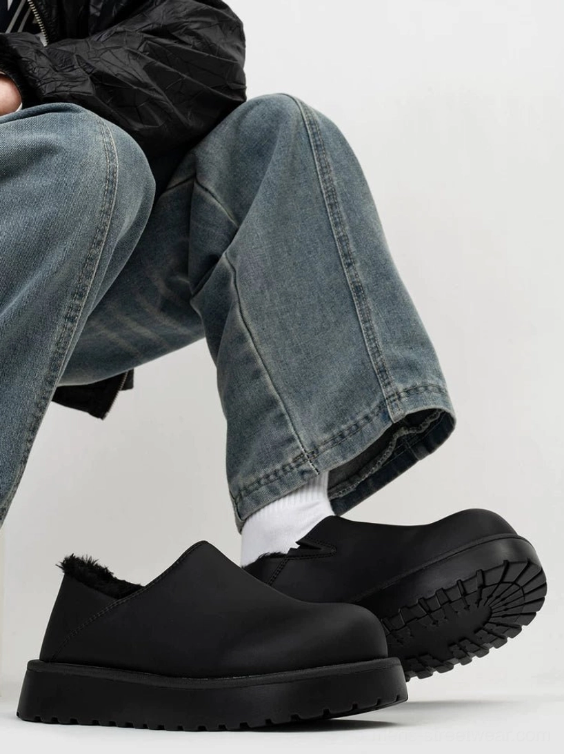 All-black shearling-lined platform slip clogs worn with jeans in a seated lifestyle view, showing the plush lining, matte upper, chunky profile, and deep tread outsole