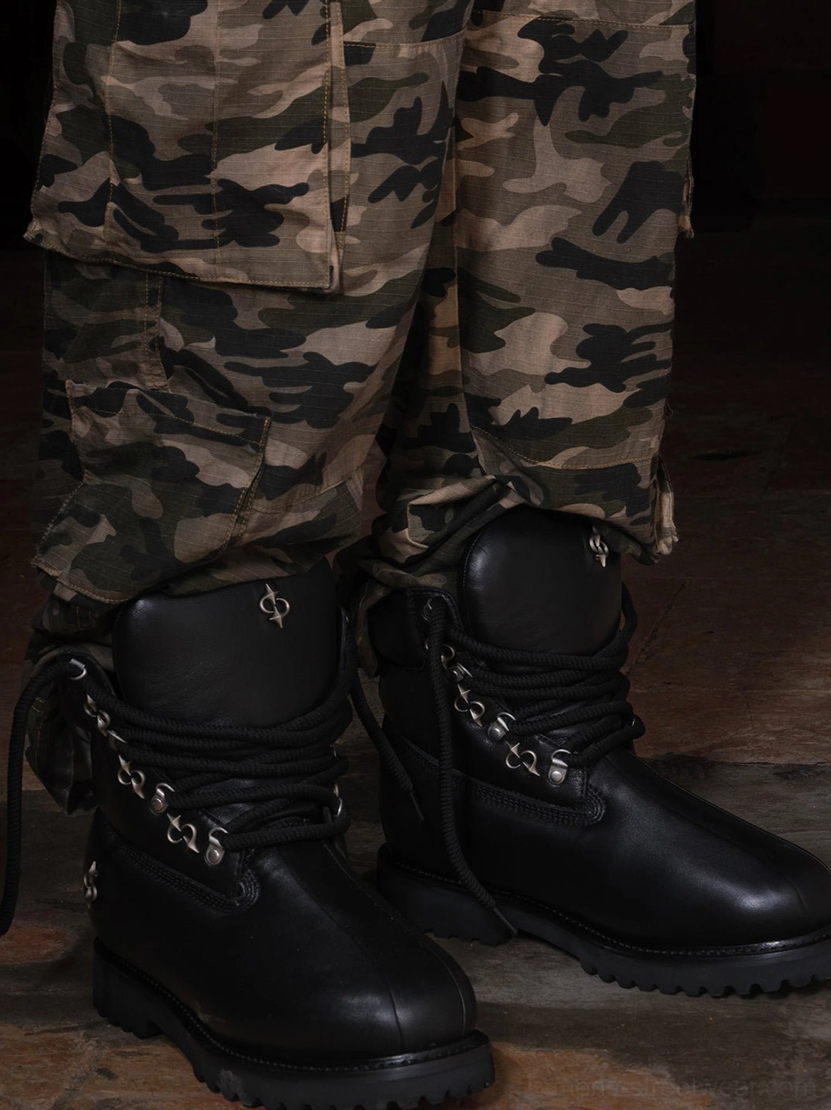 Model wearing black shearling-lined lug sole work boots with camouflage cargo pants in a dark utility streetwear outfit