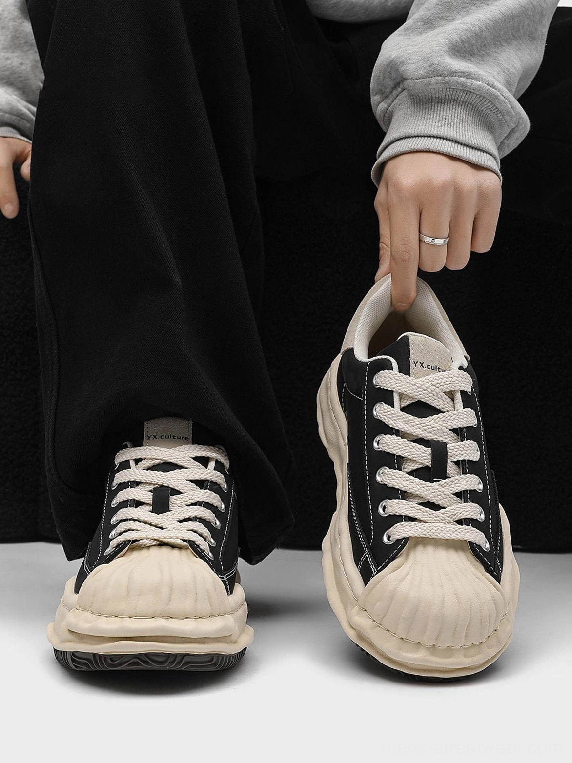 Hand-held view of a black shell-toe platform sneaker showing the interior, outsole, beige shell toe, and detailed lace panel