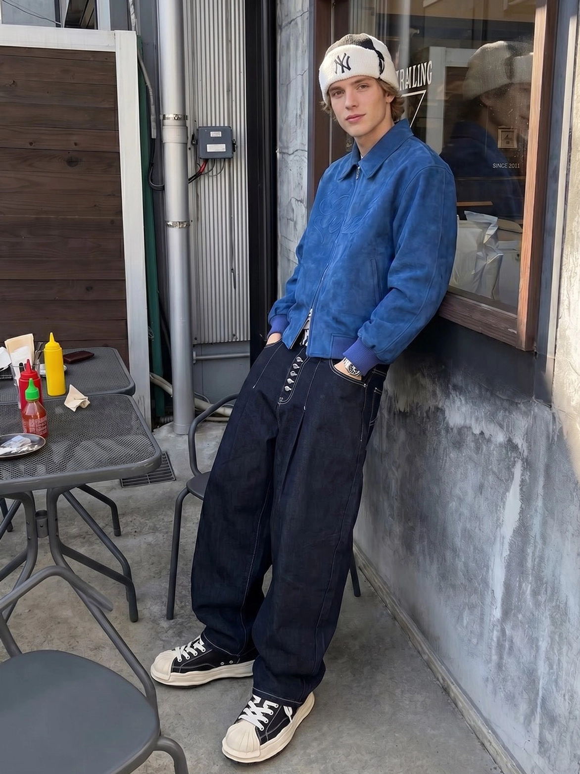 Black and beige shell-toe platform sneakers styled with wide-leg denim, blue shirt, and beanie for a downtown casual outfit