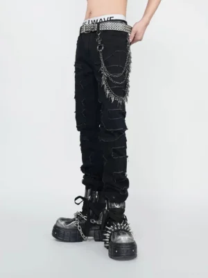 Close front view of black shredded punk jeans showing frayed denim texture, layered spiked hip chain, non-elastic waist, and chunky platform boots