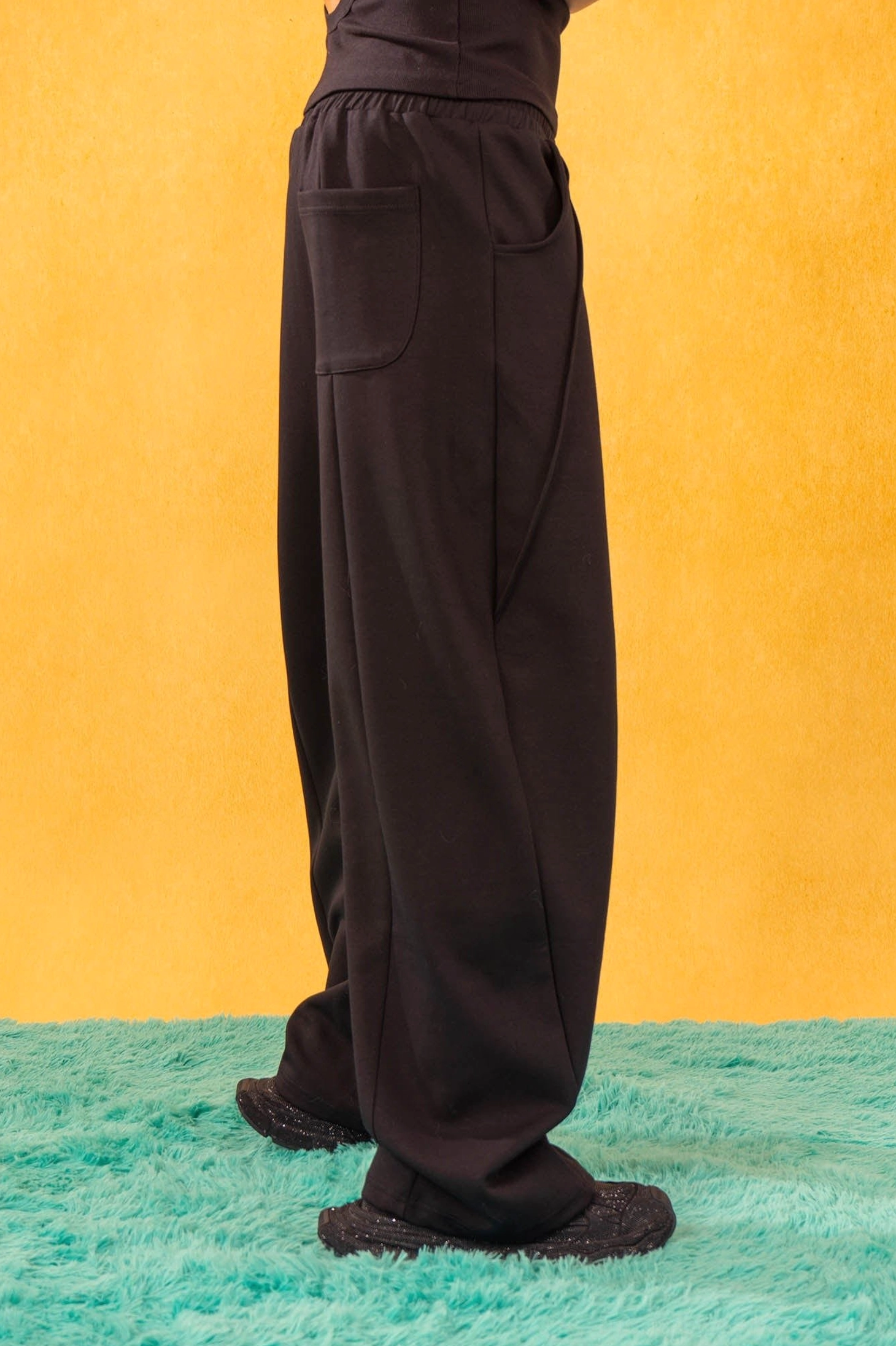 Back view of black slanted spliced wide-leg sweatpants showing patch pocket and relaxed streetwear silhouette