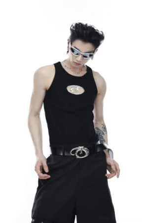 Male model wearing a black sleeveless cutout logo tank top with metallic chest emblem, silver sunglasses, layered necklaces, and Korean streetwear styling
