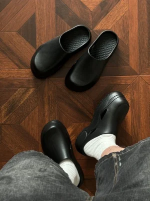 Black slip-on platform clogs with chunky 5 cm sole, honeycomb footbed, side ventilation cutouts, grey denim, and white ribbed socks