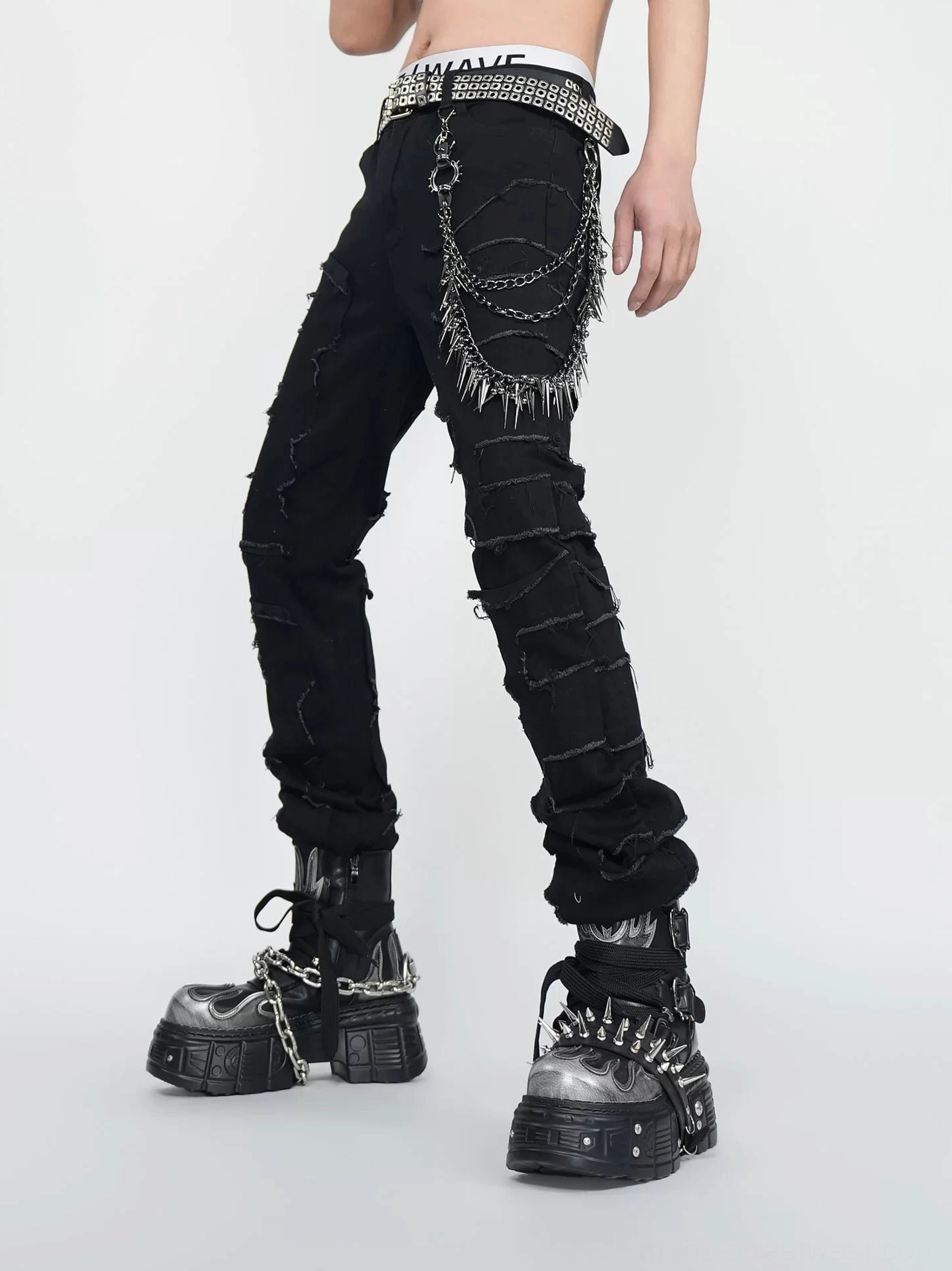Side view of black spike chain jeans with rough frayed side panels, layered metal hip chain, studded belt, and heavy platform boots
