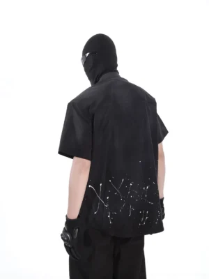 Back view of a relaxed black short sleeve splatter shirt with white paint graphics along the hem, styled for dark urban streetwear