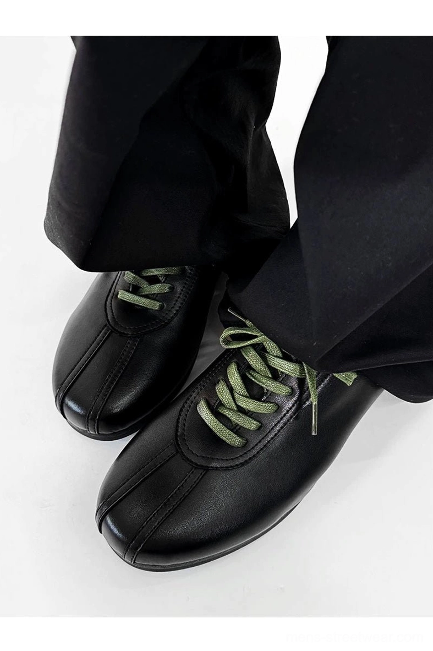 Close-up of black split-toe derby shoes highlighting split toe stitching, smooth synthetic leather, and vivid green flat laces