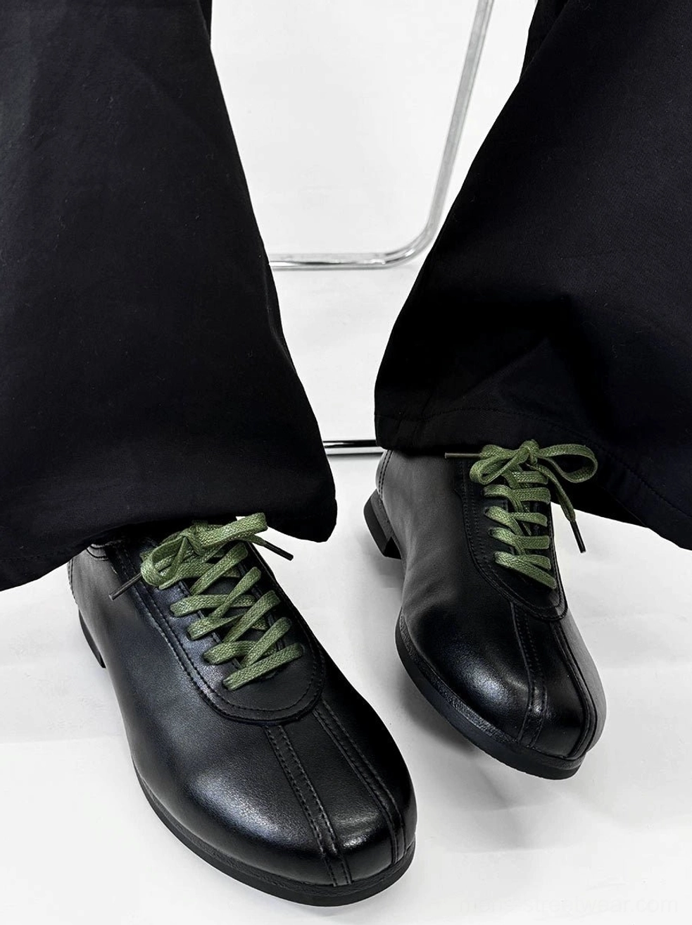 Front three-quarter view of black split-toe derby shoes with clean synthetic leather upper and contrasting green shoelaces