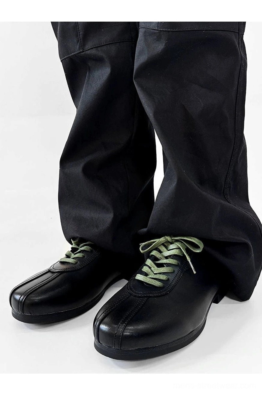 Front view of black split-toe derby shoes styled with black trousers, polished upper, split toe detail, and green laces