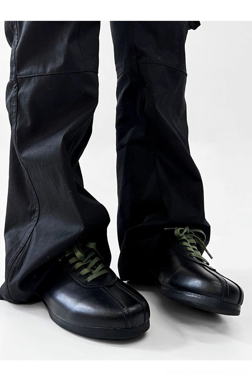 Low front view of sleek black split-toe derby shoes featuring green contrast laces and classic low derby heel