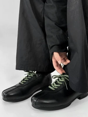 Black split-toe derby shoes with contrasting green flat laces, smooth synthetic leather upper, and modern Seoul streetwear styling