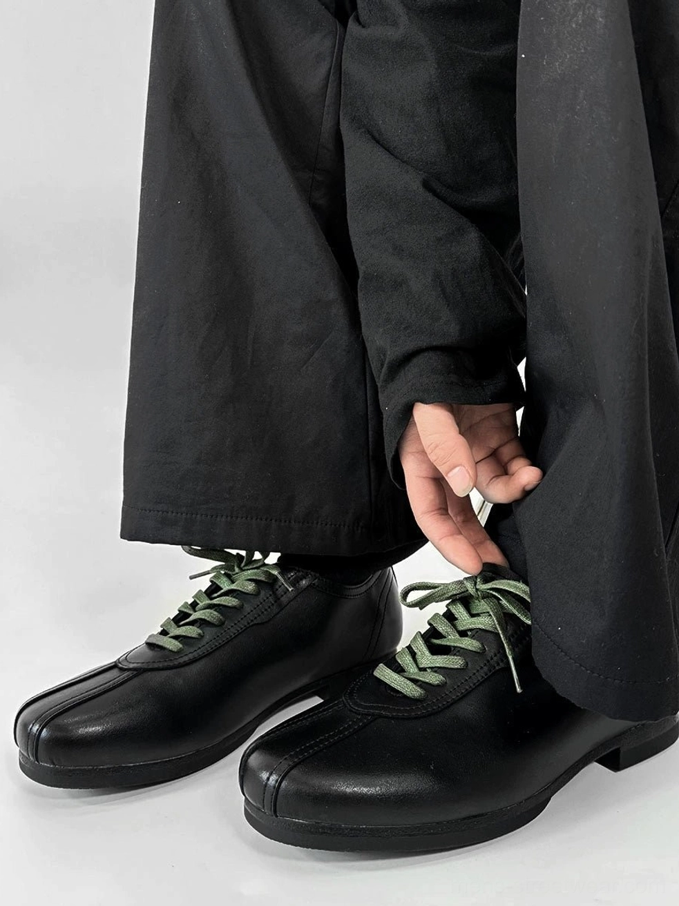 Black split-toe derby shoes with contrasting green flat laces, smooth synthetic leather upper, and modern Seoul streetwear styling