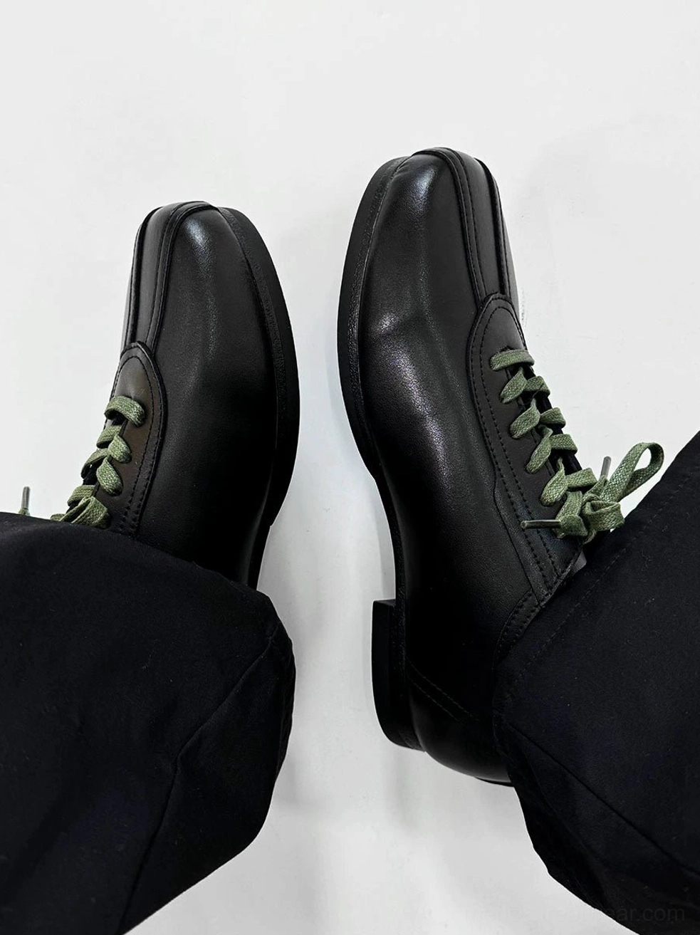 Top view of black split-toe derby shoes with smooth black upper, green laces, visible heel counter, and rubber sole