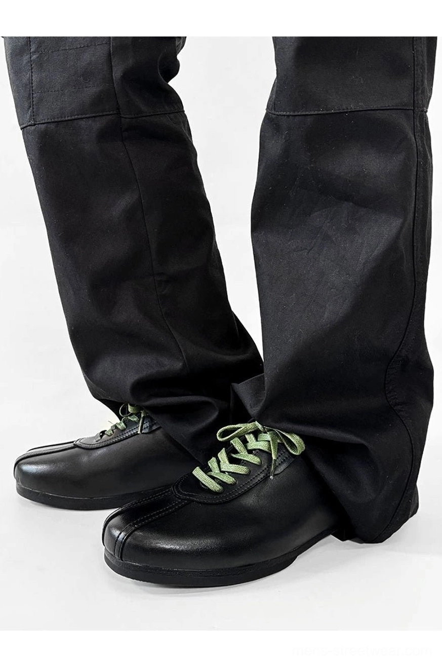 Low three-quarter side view of black split-toe derby shoes with green laces styled with wide-leg black trousers
