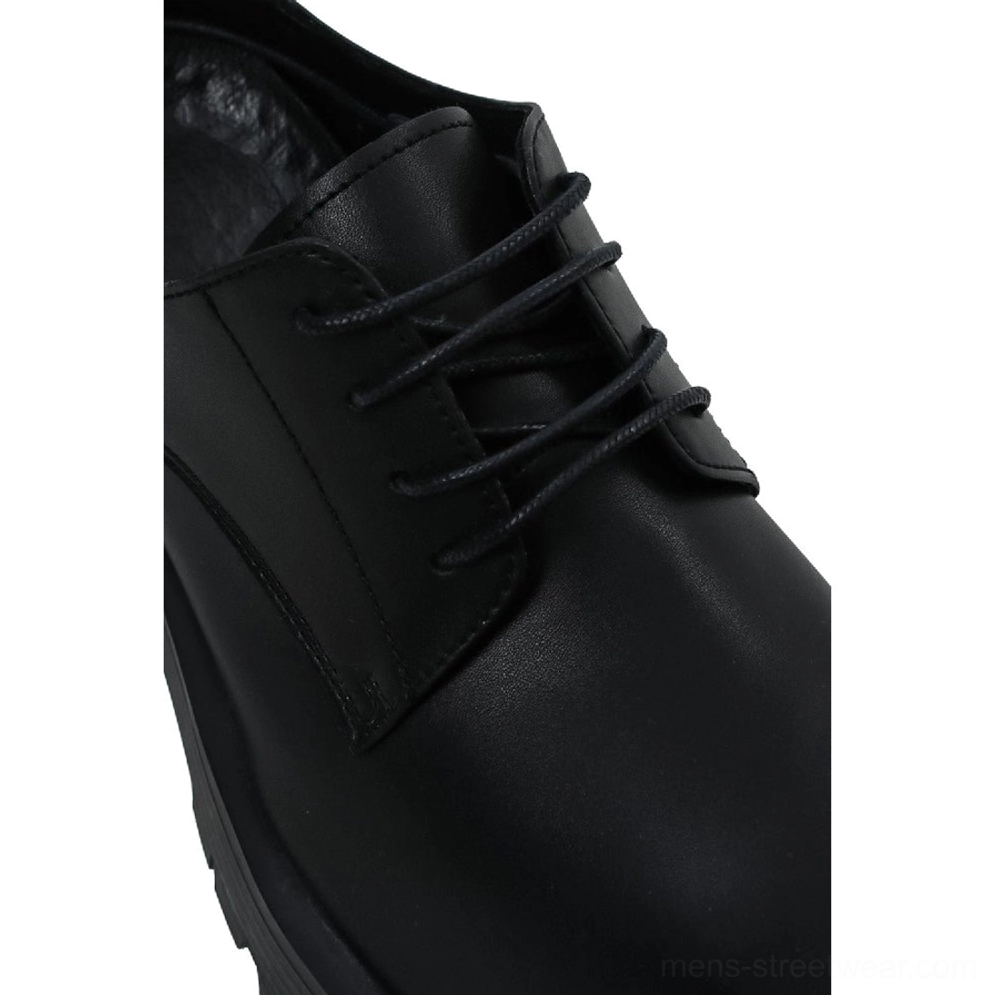 Close-up of black square-toe Derby shoes showing matte PU texture, round black laces, vamp overlay, and neat stitching