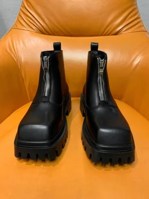 Black square-toe front-zip platform boots displayed on a bright orange leather chair, showing the smooth upper and chunky lug sole