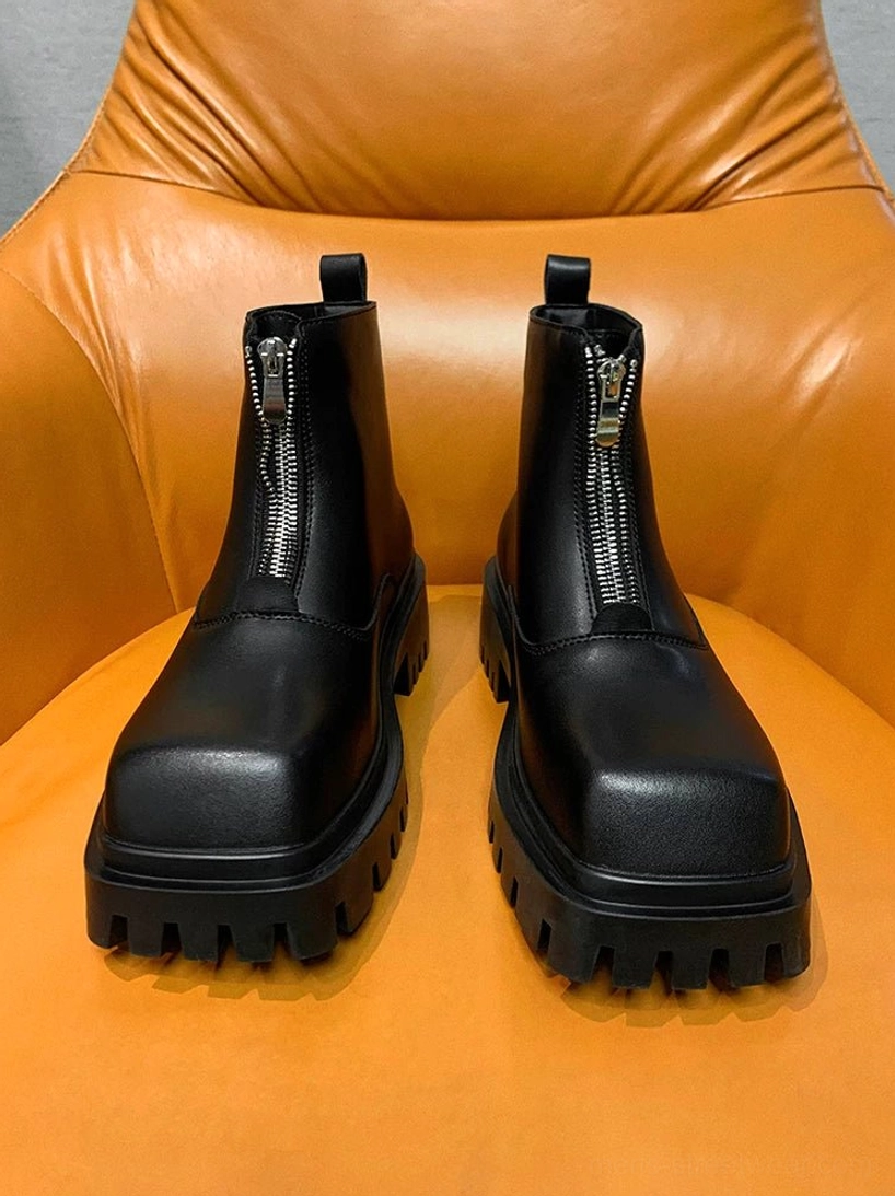 Black square-toe front-zip platform boots displayed on a bright orange leather chair, showing the smooth upper and chunky lug sole
